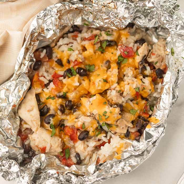 A chicken enchilada foil packet meal that has been opened up in the foil and has been topped with the shredded cheese. 