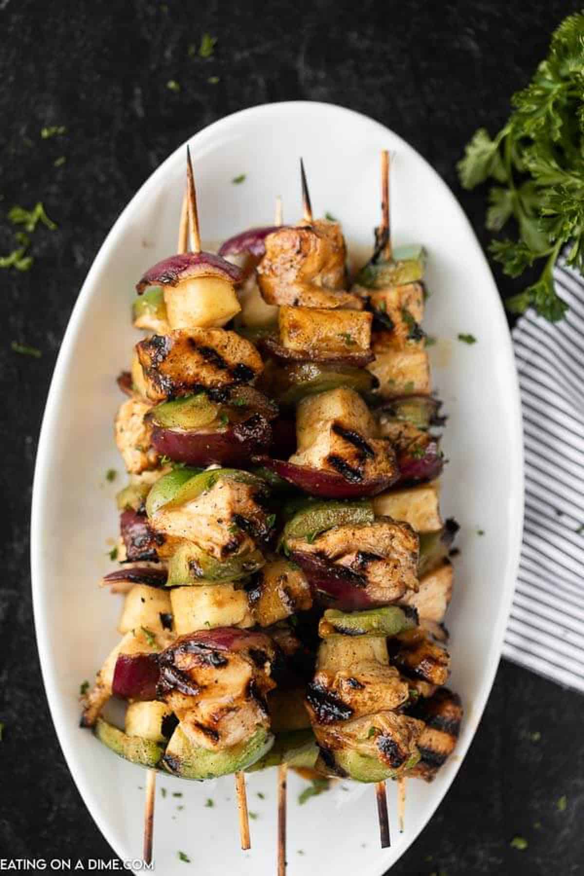 5 cooked chicken kabobs with veggies on a white platter. 
