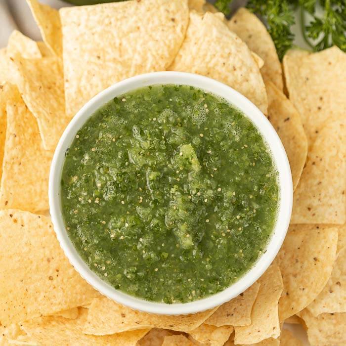 A white bowl of salsa verde surrounded by tortilla chips 