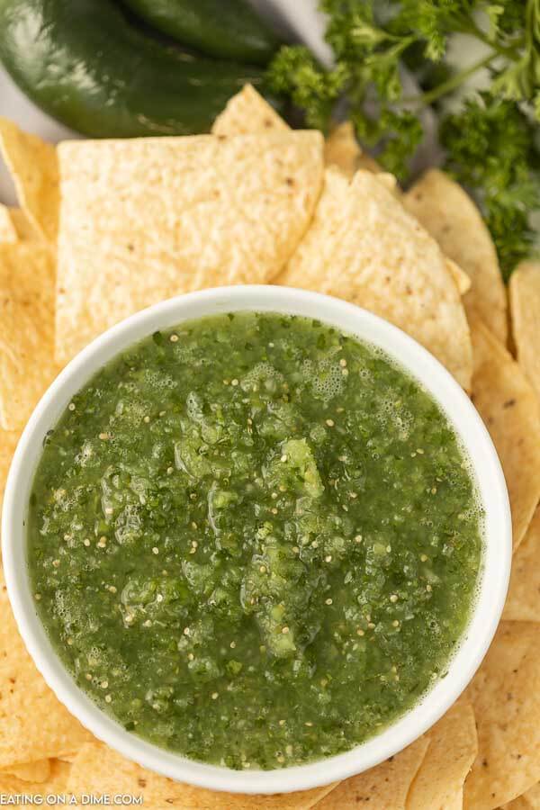 A large bowl of salsa verde surrounded by tortilla chips 