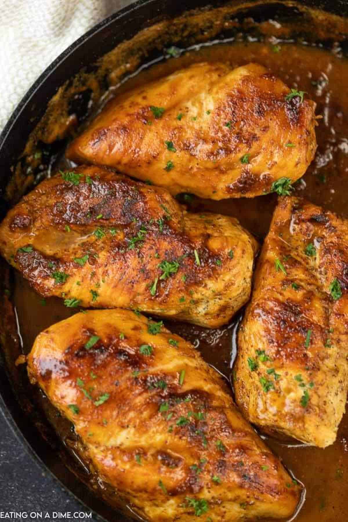 Four seasoned and grilled chicken breasts sizzle in a skillet, garnished with chopped parsley. Coated in a golden-brown honey mustard glaze sprinkled with spices, they rest in a rich, brown sauce perfect for this delectable chicken recipe.