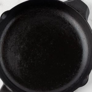 A close-up view of an empty black cast iron skillet on a white surface, showing its smooth and seasoned interior—an ideal example of how to season a cast iron skillet for lasting nonstick performance.