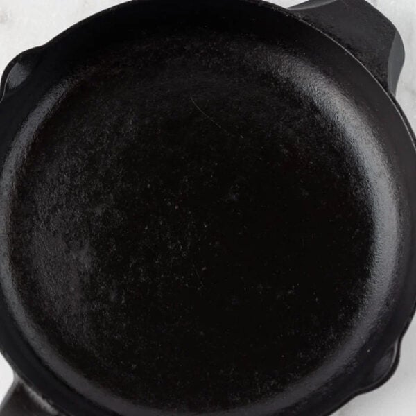 A close-up view of an empty black cast iron skillet on a white surface, showing its smooth and seasoned interior—an ideal example of how to season a cast iron skillet for lasting nonstick performance.