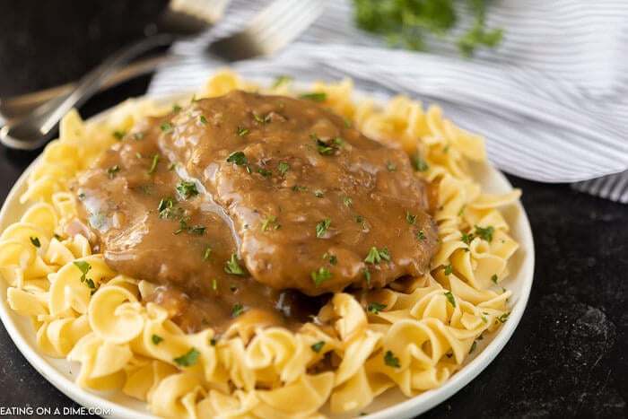 cube steak served over egg noodles on a white plate