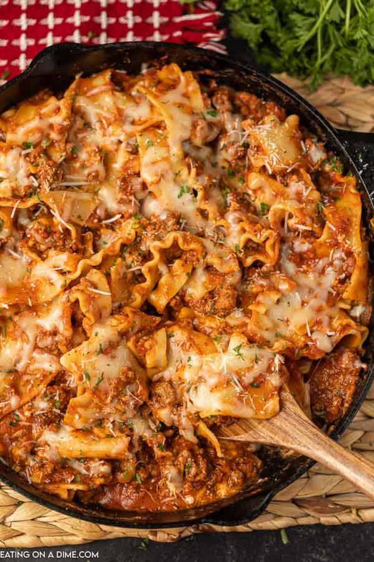 Lasagna in a cast iron skillet with a wooden spoon scooping out a portion of it for serving 