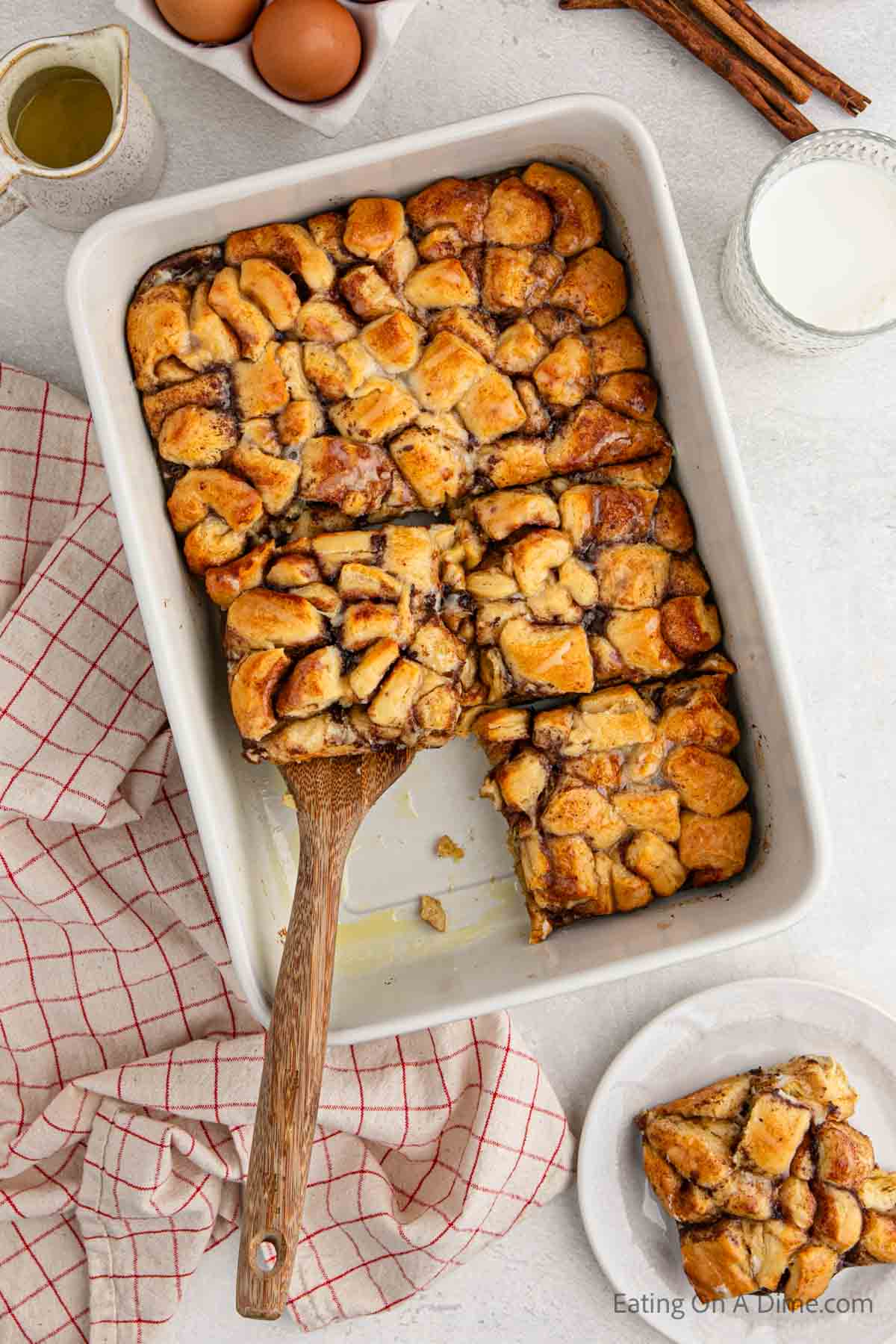 Close up image of cinnamon roll french toast casserole in a baking dish with a wooden spatula
