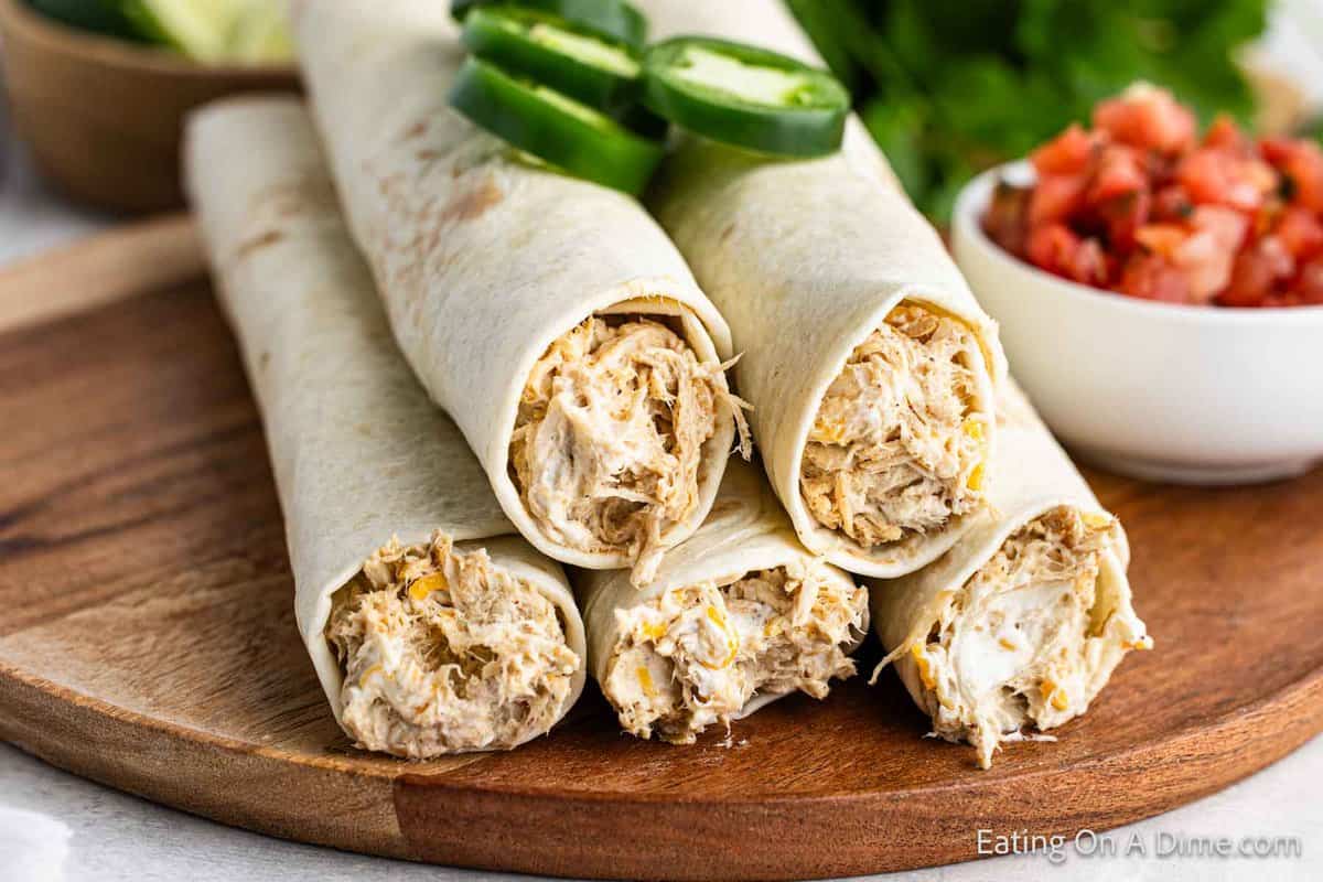 Chicken Taquitos stacked on a wooden board with a side of salsa