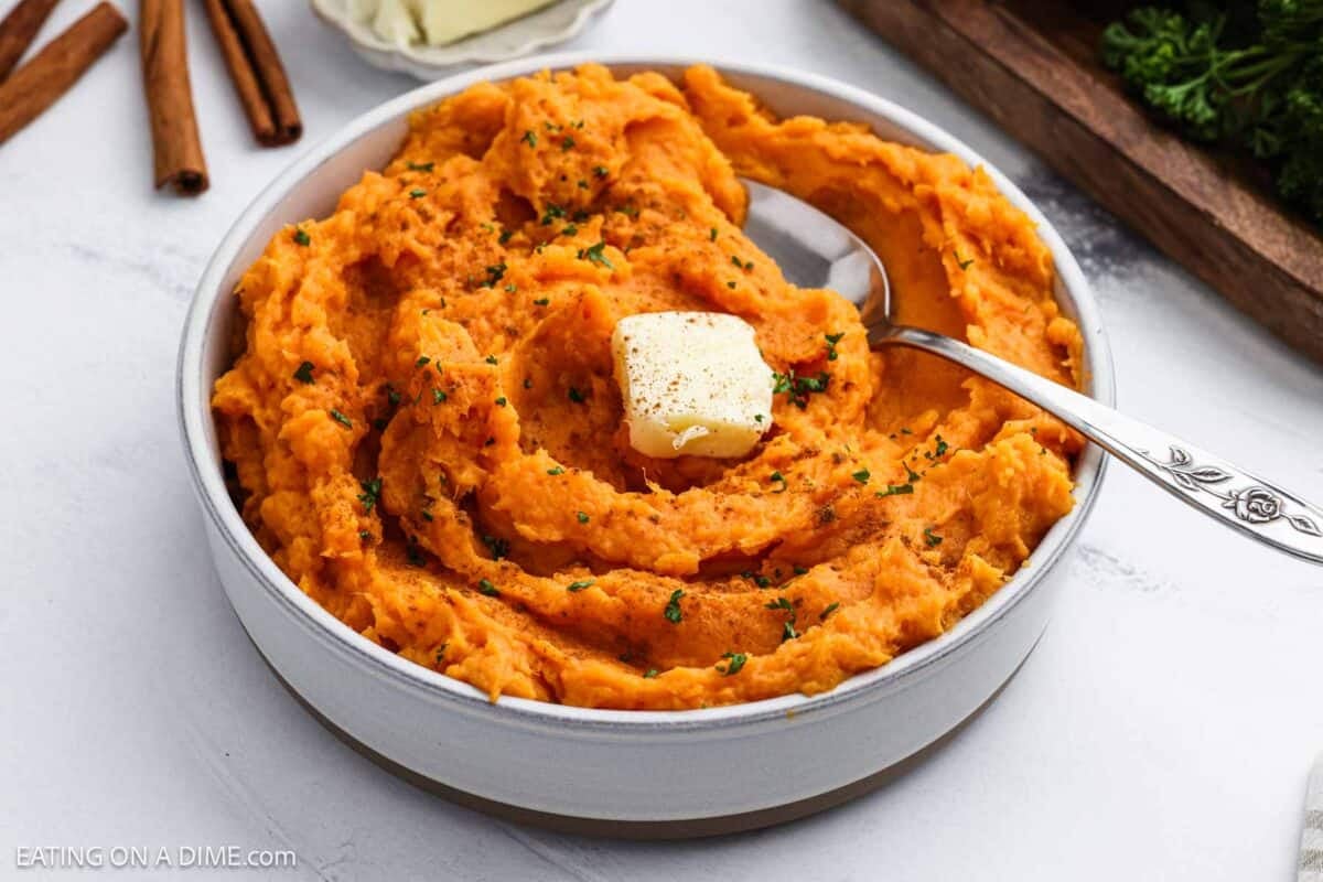 Mashed sweet potatoes in a bowl topped with a slice of butter.