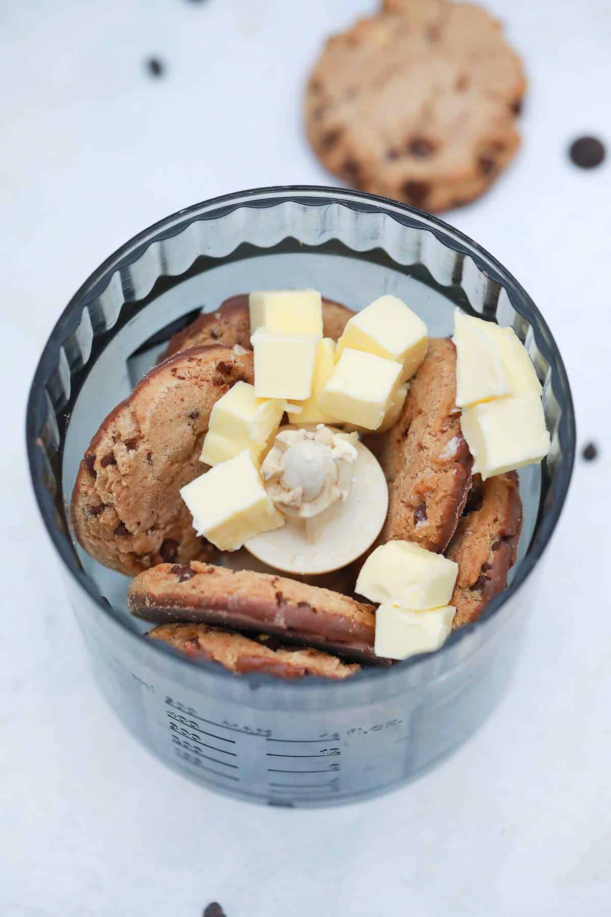 Chocolate chips cookies and butter in a food processor.