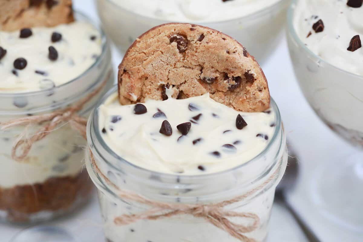 Mini no bake chocolate chip cookie cheesecake in a clear mason jar topped with a chocolate chip cookie.