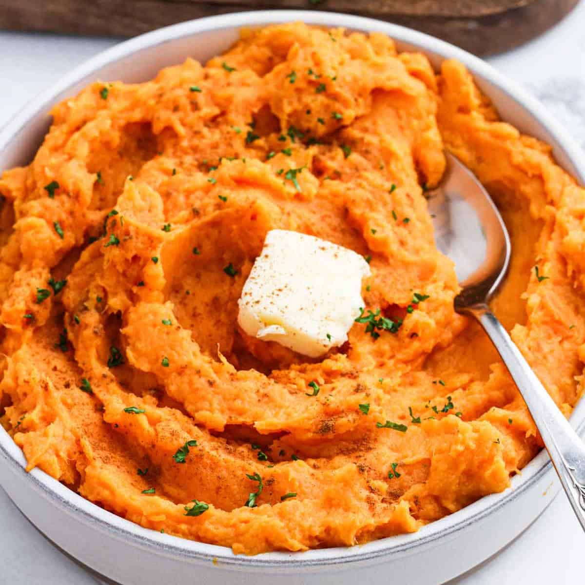 Mashed sweet potatoes topped with a slice of butter in a bowl.