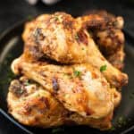 A close-up of several seasoned, cooked Air Fryer Drumsticks stacked on a black plate, garnished with chopped parsley.