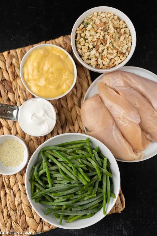 Close up image of ingredients of chicken and stuffing. It includes uncooked stuffing, green beans, chicken breast, cream of chicken soup, sour cream and seasoning. 