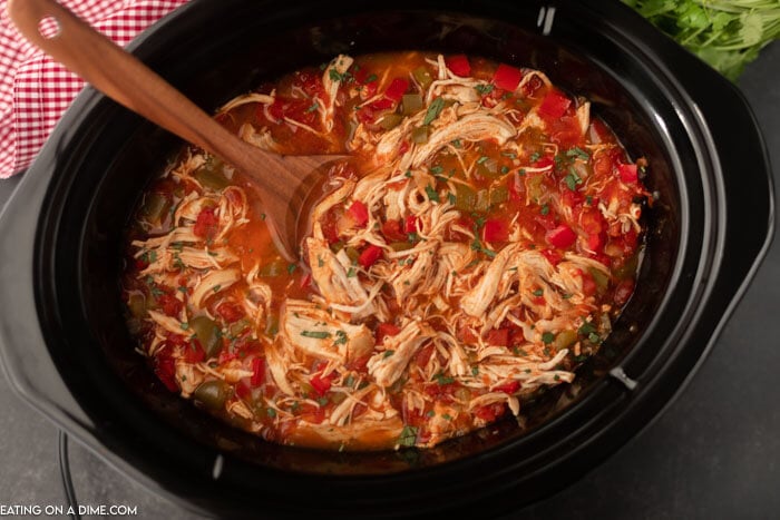 Chicken fajita soup cooked in a crock pot and topped with fresh chopped cilantro with a wooden spoon in it 