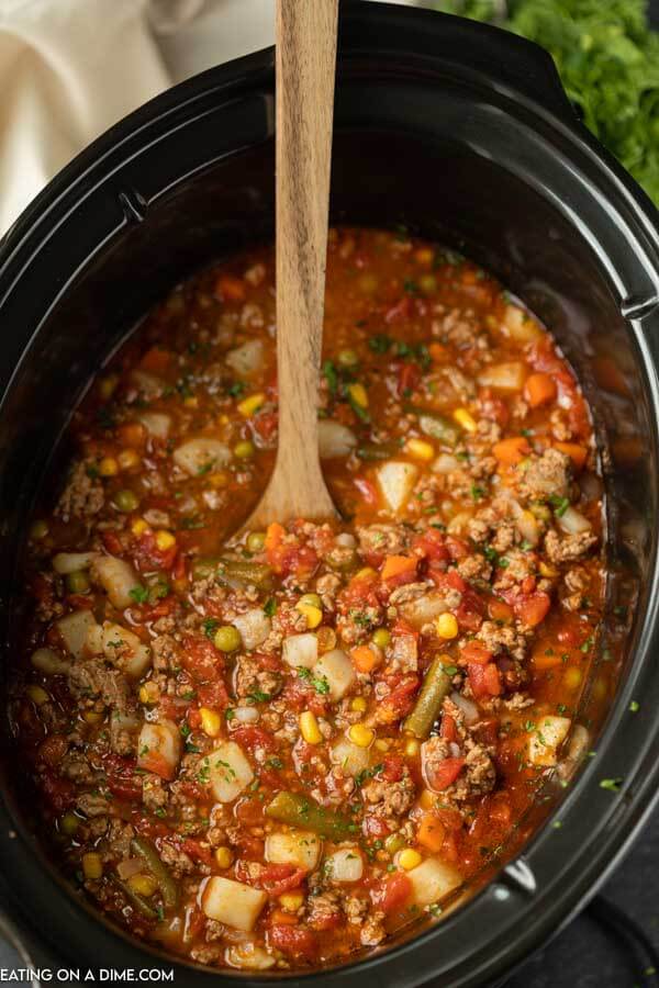 Una pentola di coccio piena di questa zuppa di manzo vegetale con un cucchiaio di legno nella zuppa. 