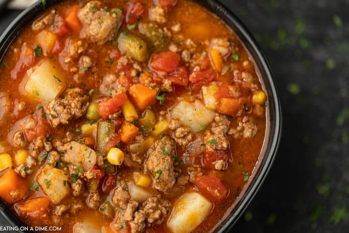 A black bowl full of vegetable beef soup topped with fresh parsley 