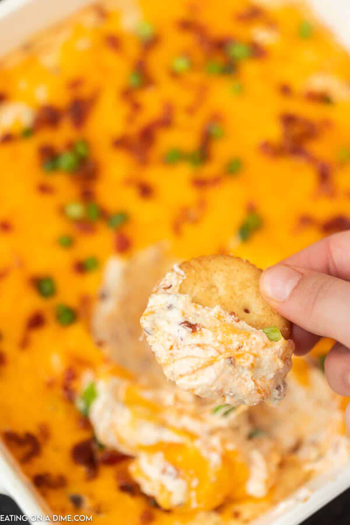 A Cracker with some of the crack dip on it being scooped out of the pan of crack dip 