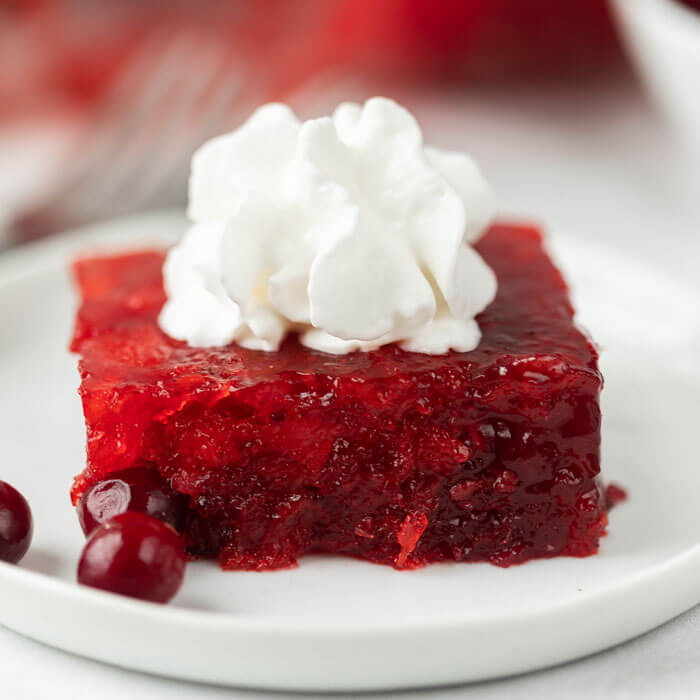 Slice of cranberry jello salad on a plate topped with whipped cream