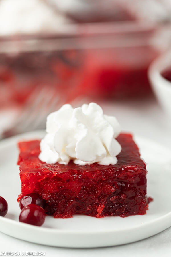 cranberry salad cut into square on a plate and topped with whipped cream.