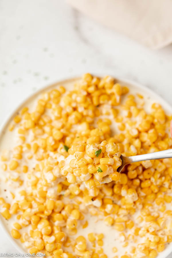 Close up image of creamed corn in a bowl with a serving on a spoon.