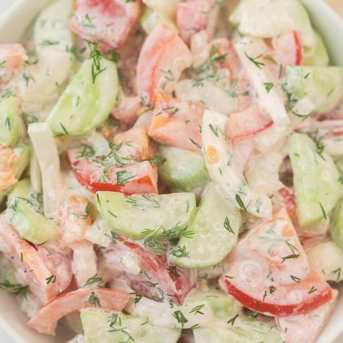 closeup photo of creamy cucumber and tomato salad in a white bowl.