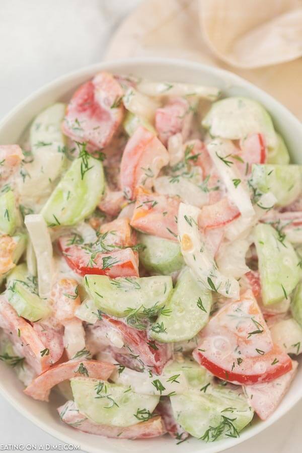 closeup photo of creamy cucumber and tomato salad in a white bowl.