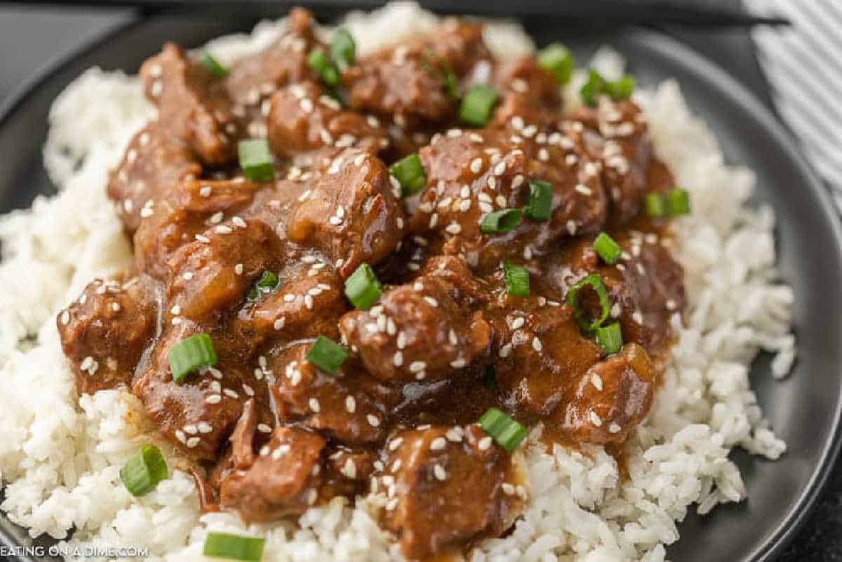 Teriyaki beef over white rice on a plate topped with green onions and sesame seeds.