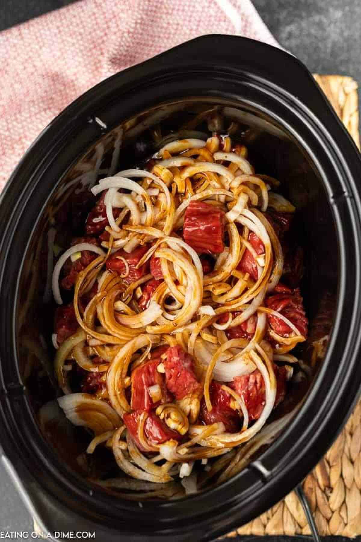 Flank steak, sliced onions and teriyaki sauce in a crock pot.