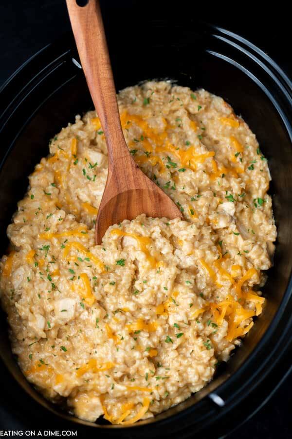 Cheesy Chicken and Rice in a crock pot with a wooden spoon in the middle of it. 