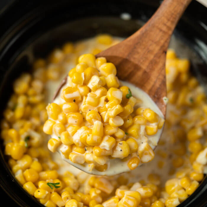 Creamed corn in crockpot with a serving on a wooden spoon. 