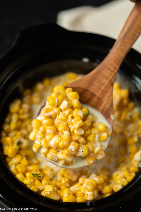 Close up image of creamed corn in the crock pot with a serving on a wooden spoon.