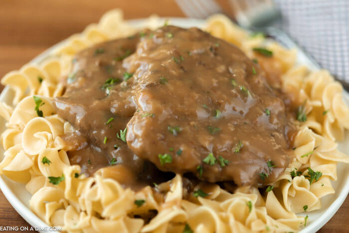 white plate with egg noodles topped with cube steak and gravy
