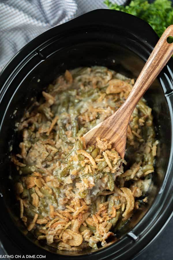 Green bean casserole in a crock pot with a wooden spoon in it. 