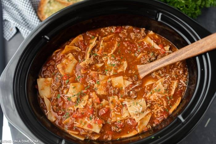 You have to try this easy crock pot lasagna soup recipe! A lasagna soup recipe that tastes just like lasagna without all the work. a crock pot full of this lasagna soup with a wooden spoon in it