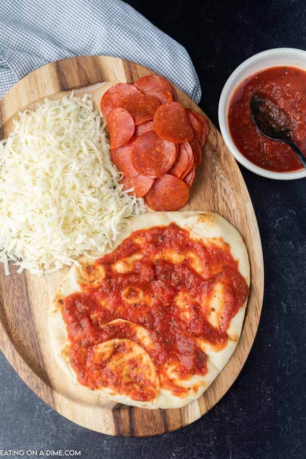 Close up image of ingredients for pepperoni pizza - cheese, pepperoni, flatbread, and pizza sauce. 