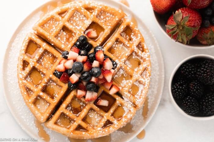 Gluten Free Waffles topped with fresh fruit and powdered sugar with a bowl of strawberries and blackberries. 