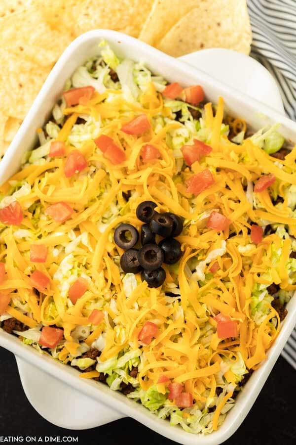 baking dish with ground beef taco dip topped with cheese, tomato, olives and lettuce