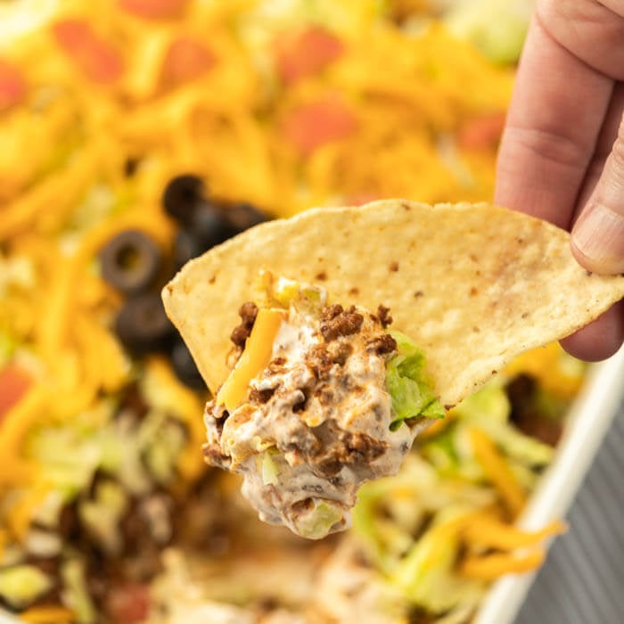 baking dish with taco dip being scooped with a chip