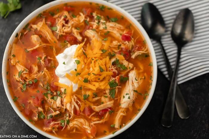 Close up image of a bowl of chicken fajita soup in a white bowl white two black spoons. 
