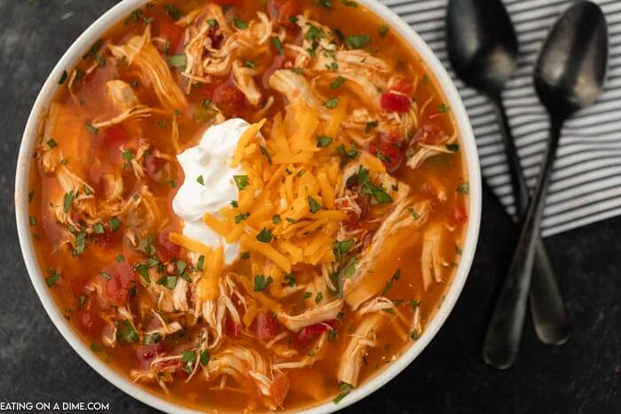 Close up image of a bowl chicken fajita soup in a white bowl with two black spoons. 