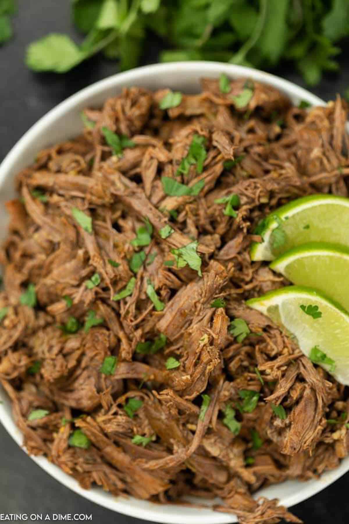 A large bowl of Mexican Shredded Beef topped with cilantro and limes. 