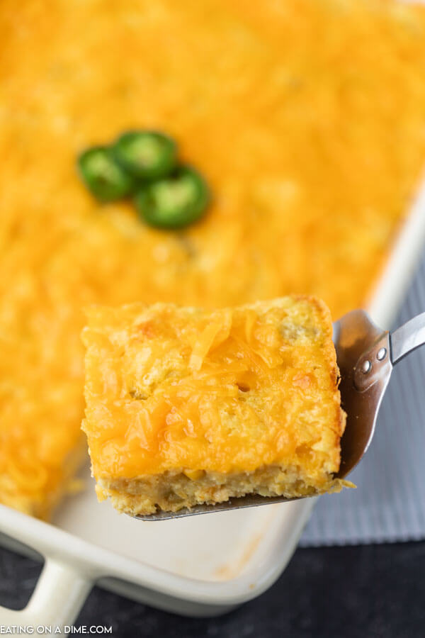 Close up image of corn casserole in baking dish with a serving on a spatula. 