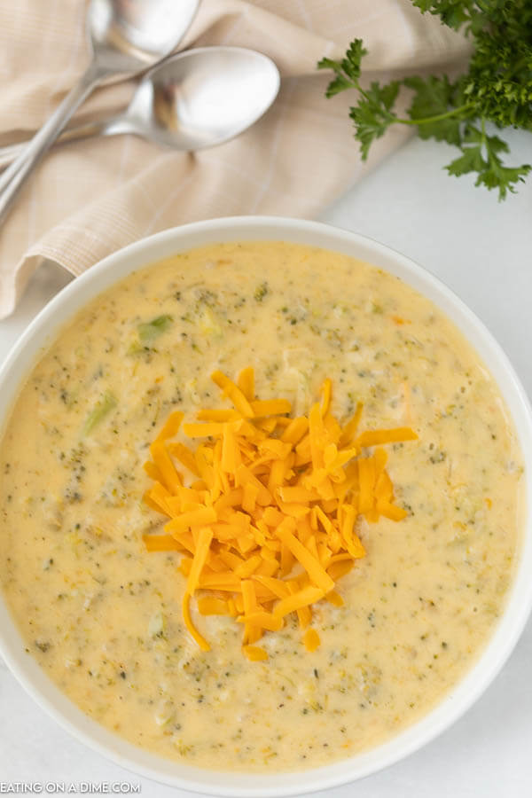 A bowl of broccoli cheese soup topped with shredded cheddar cheese with 2 spoons behind it. 