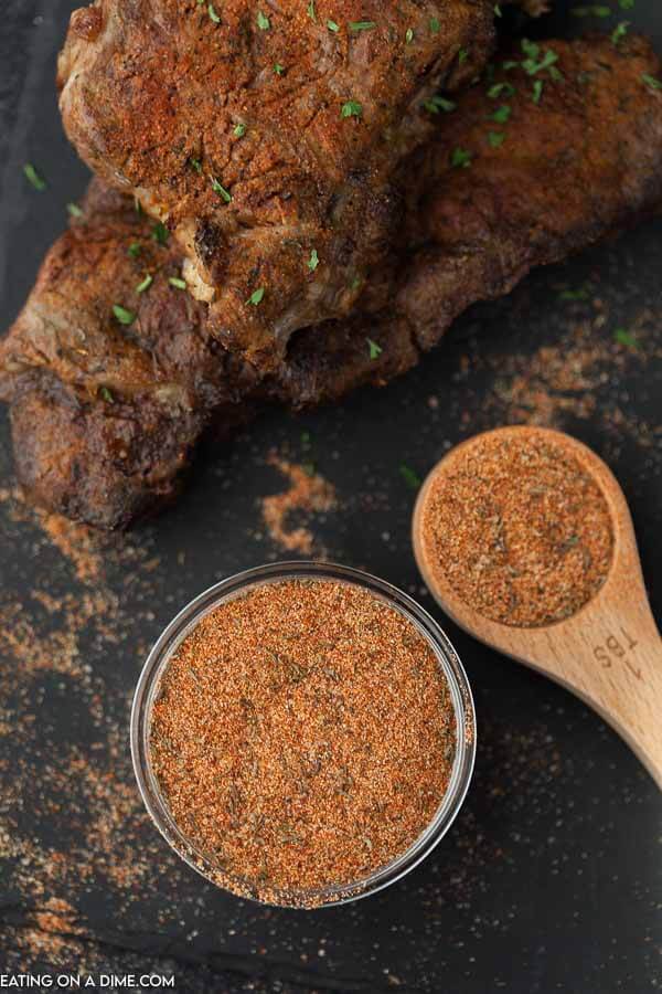 A bowl and 1 Tbsp of Steak Seasoning mix sitting on a black plater with 2 seasoned and cooked steaks 