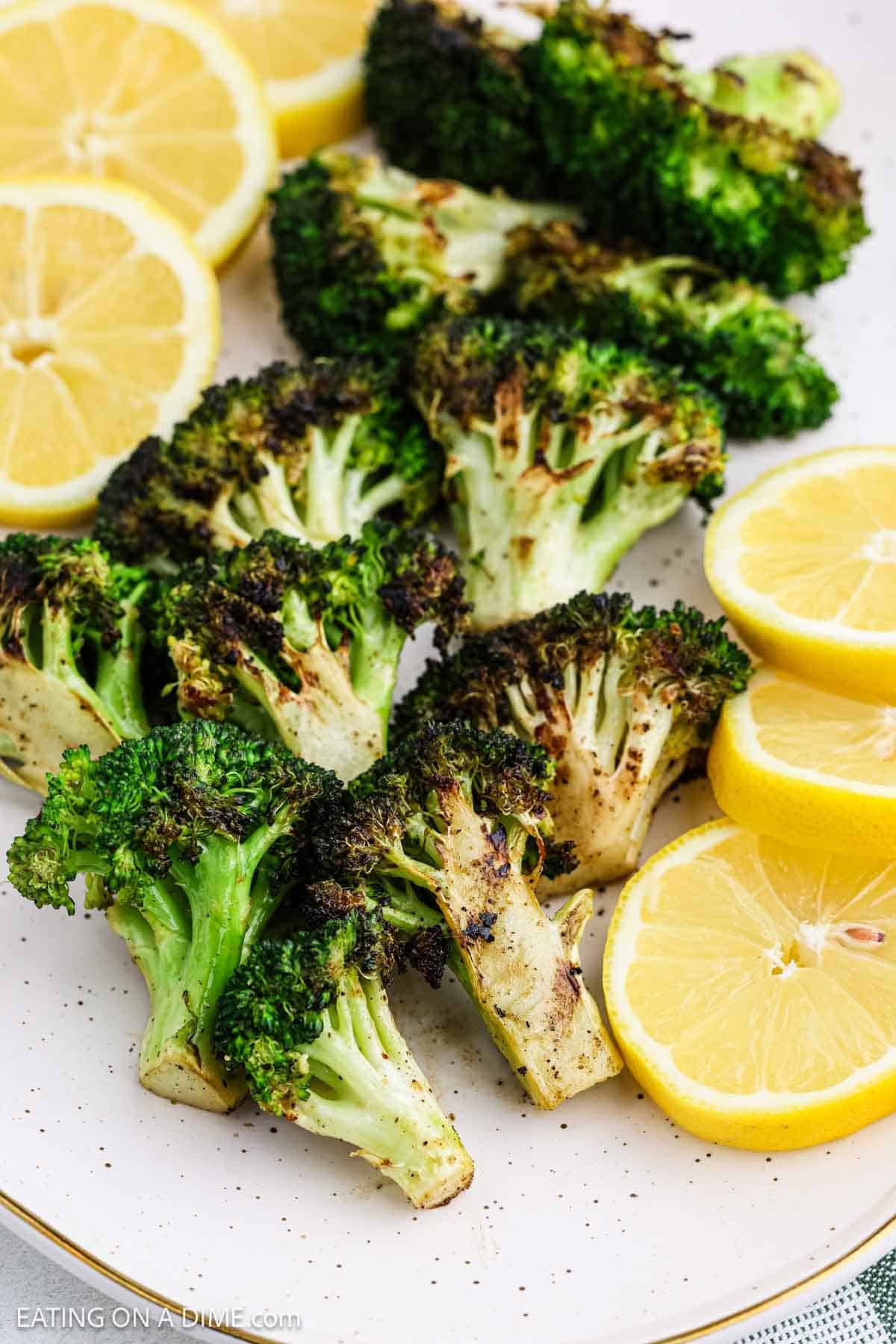 Grilled broccoli florets with char marks are arranged on a plate alongside fresh, bright yellow lemon slices for a vibrant and flavorful presentation.