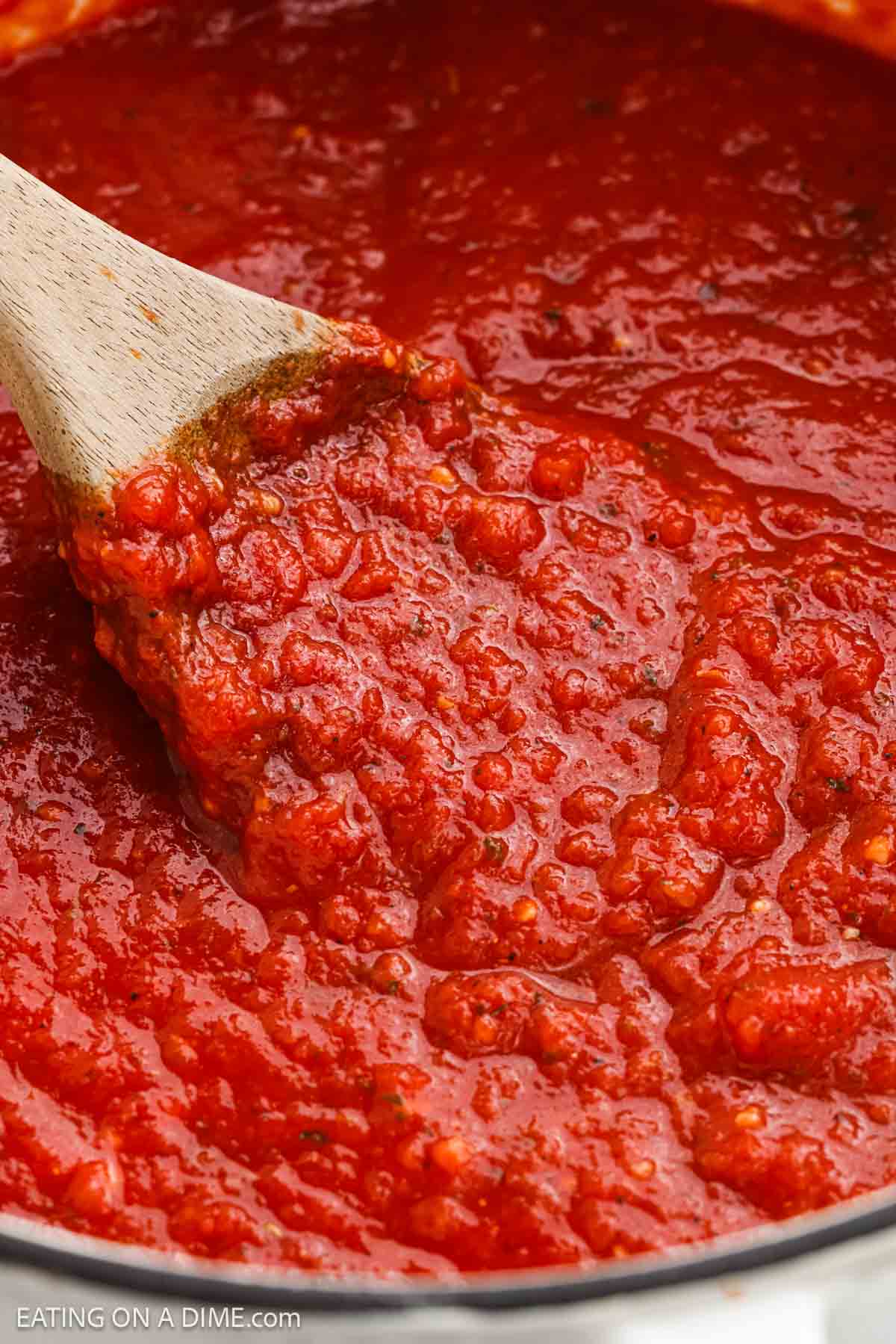 Close up image of red sauce in a large pot with a wooden spoon.