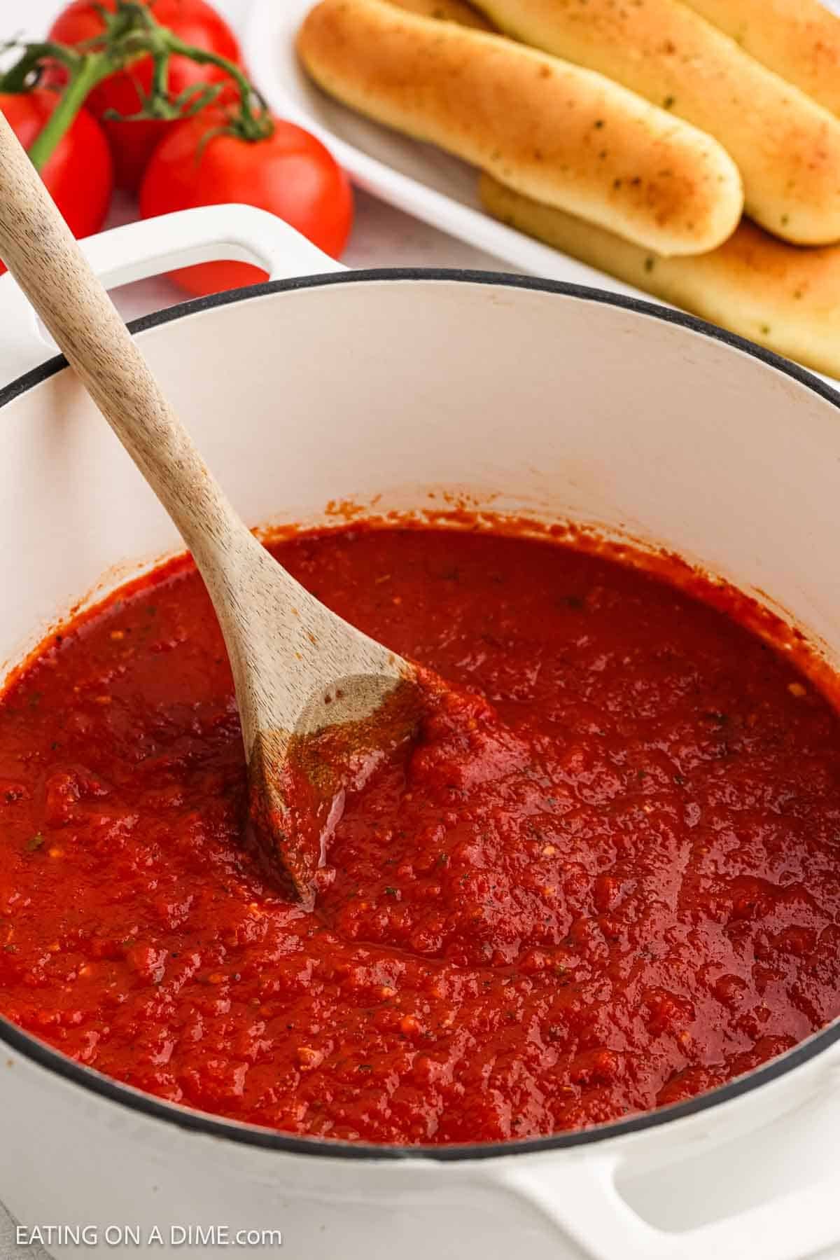 Red sauce in a large pot with a wooden spoon.