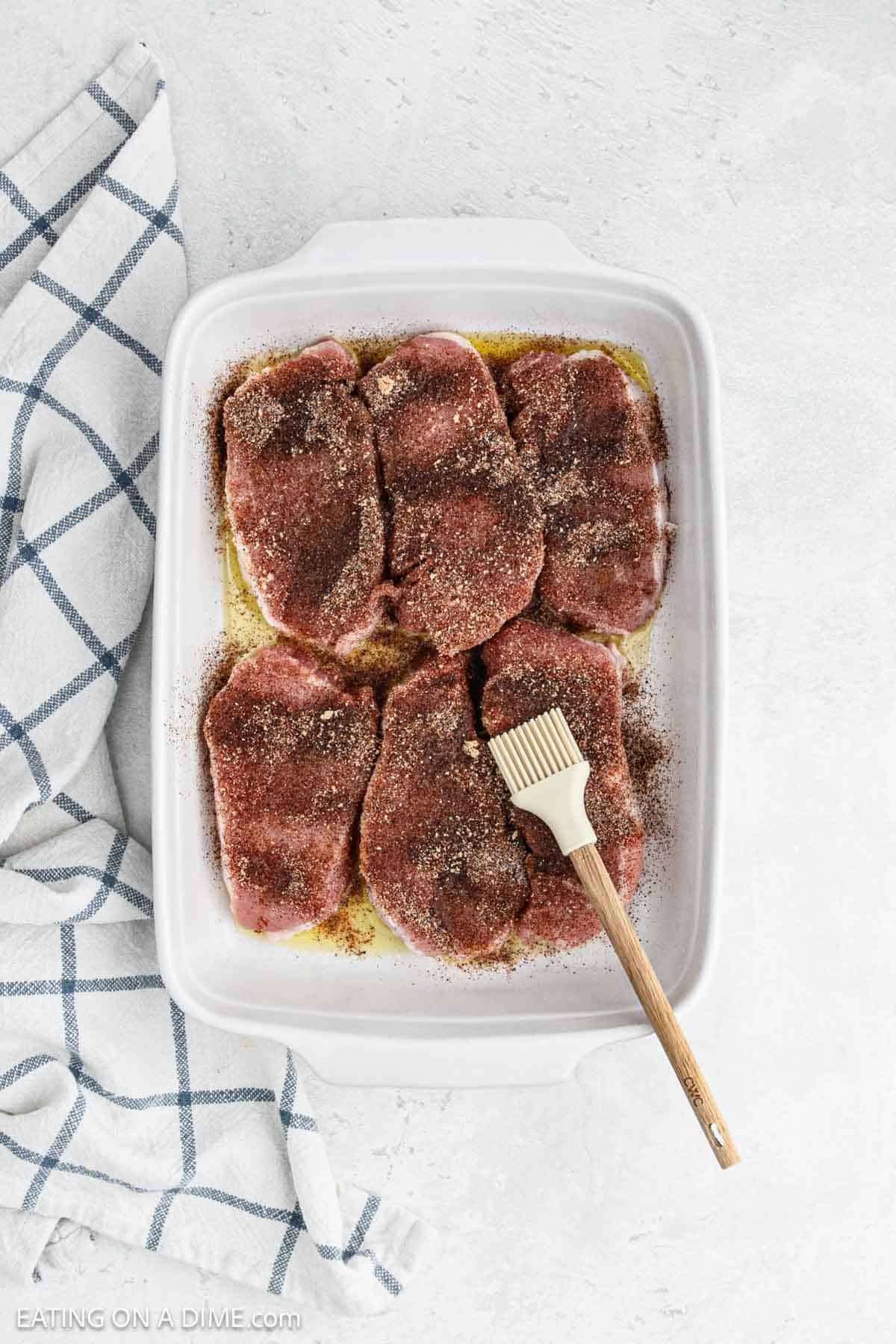 Pork chops in a baking dish topped with oil and the seasoning mixture. 
