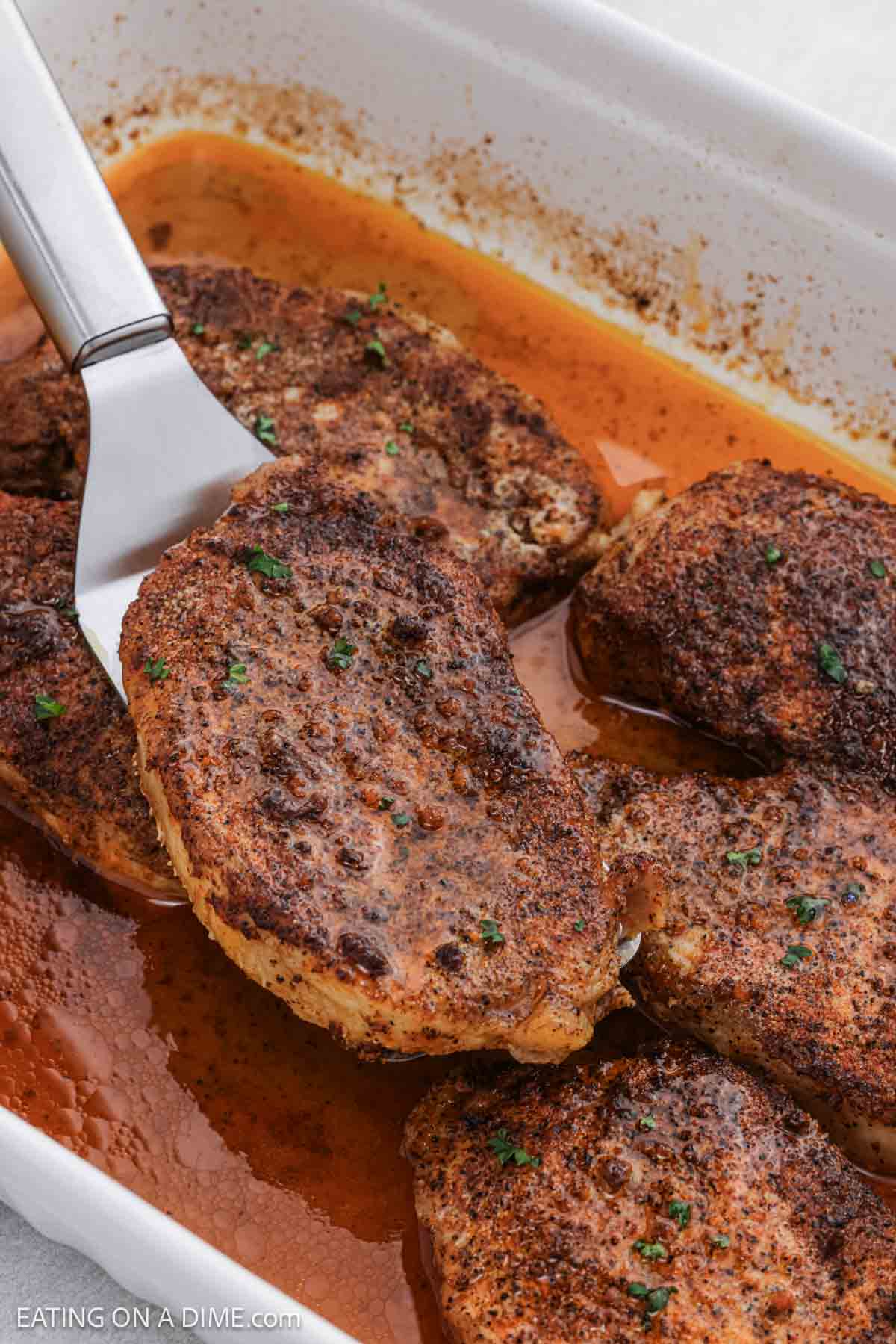 Cooked pork chops in a baking dish with one pork chops on a spatula. 