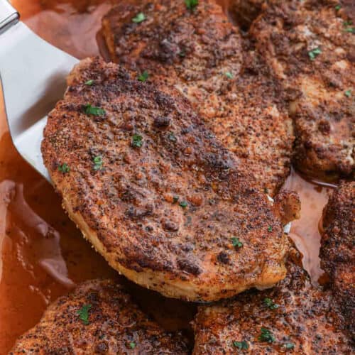 Cooked pork chops in a baking dish with a serving on a spatula.